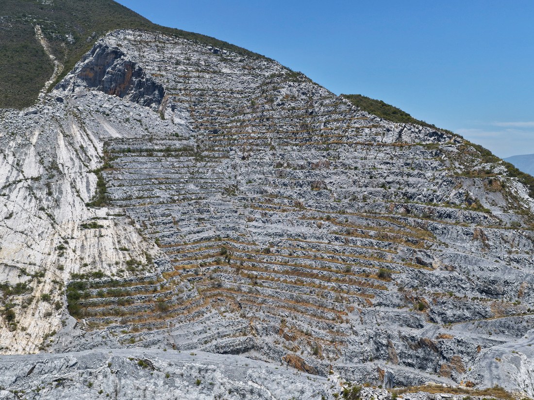 Cantera de caliza con bancos escalonados en ladera, vista desde el aire